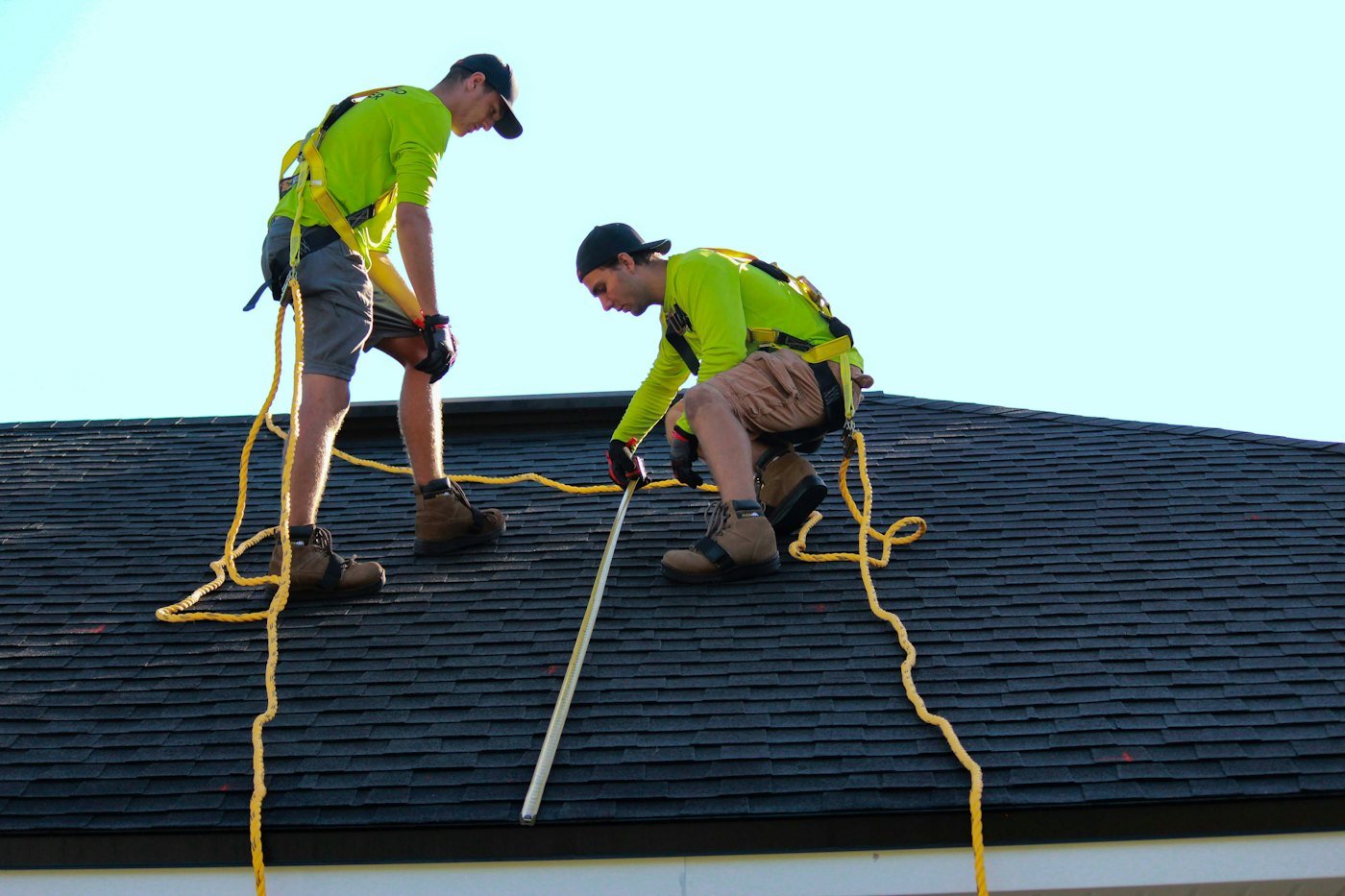 Roofing crew in safety gear working on a shingle roof