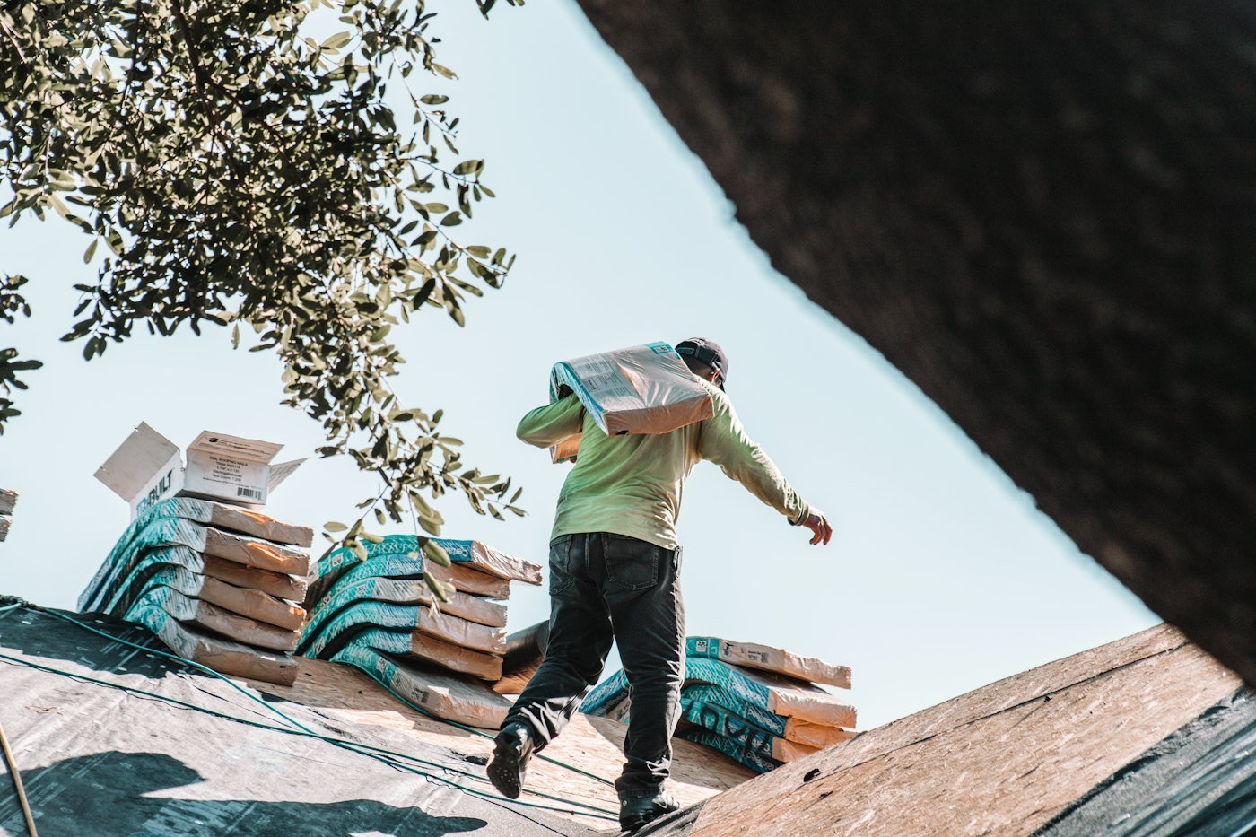 Roofer carrying bundles of shingles on a roof